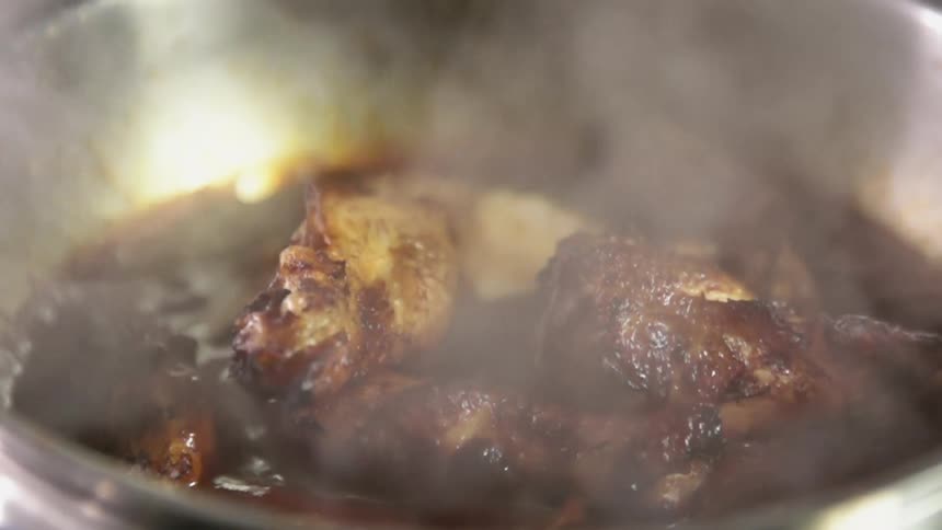 Meat simmers in sauce in a metal pan