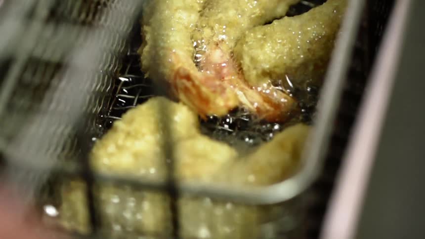 Tempura shrimp frying in hot oil as the fryer basket shakes