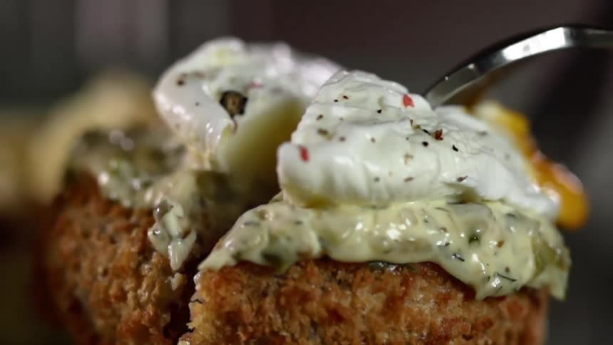 A sausage patty topped with a poached egg is cut in half and pulled apart with a fork