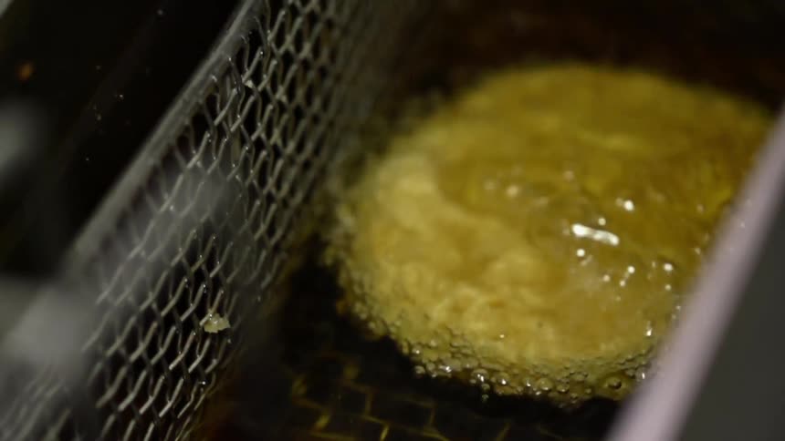 A breaded patty in a fryer basket is slowly submerged in hot oil to cook it