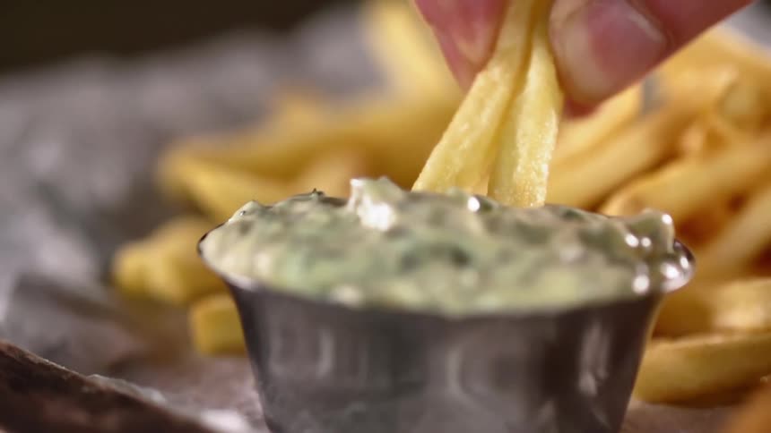 A white person dips a couple of french fries into a dipping sauce