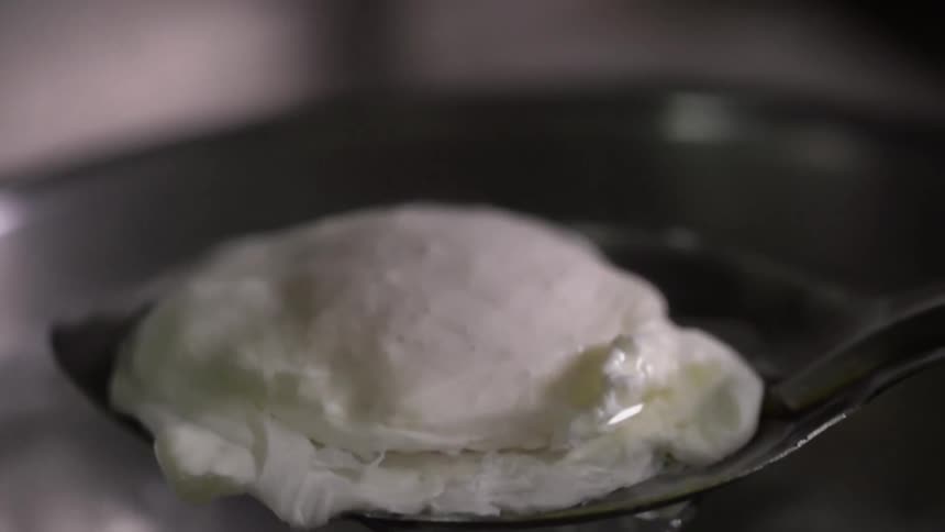 A cook lifts a cooked egg out of pan filled with water