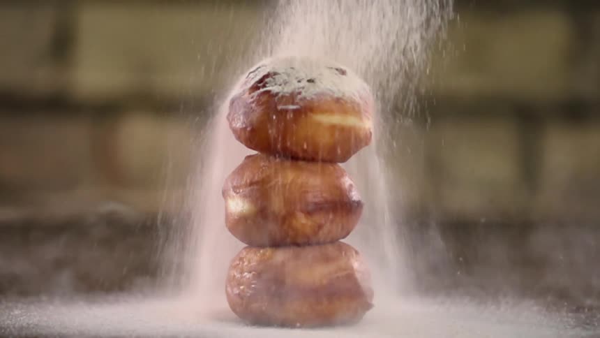 Powdered sugar is poured on the stack of donuts