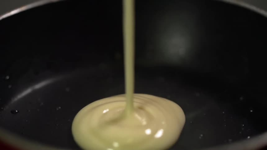 Yellow batter pouring into a black pan pools on the bottom surface