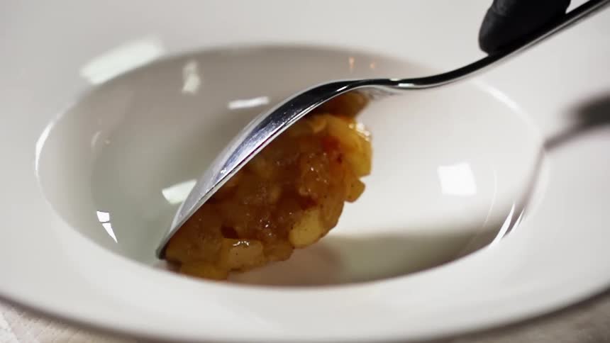 Food is dished into a white ceramic bowl by a gloved hand