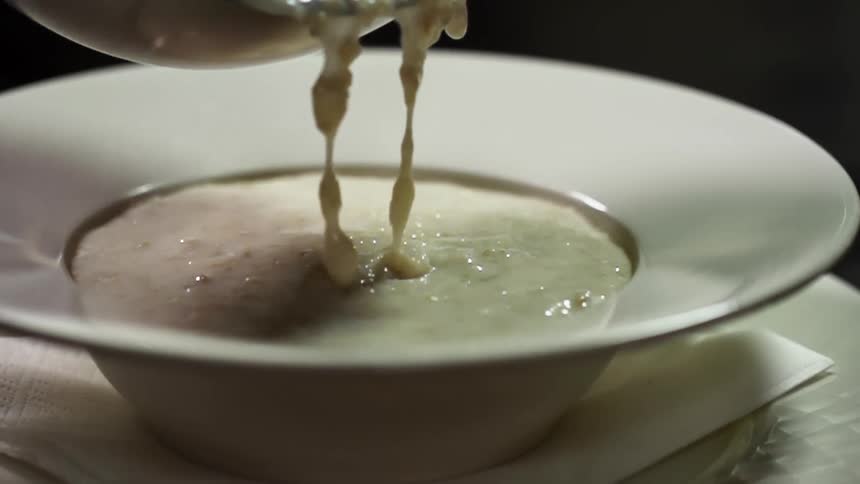 Chowder being poured into a bowl on a table with a spoon