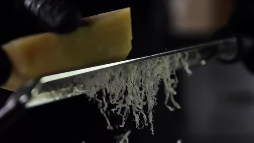 A person is grating a large piece of cheese