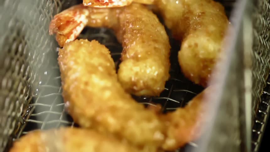 A basket containing breaded shrimp is removed from a deep fryer