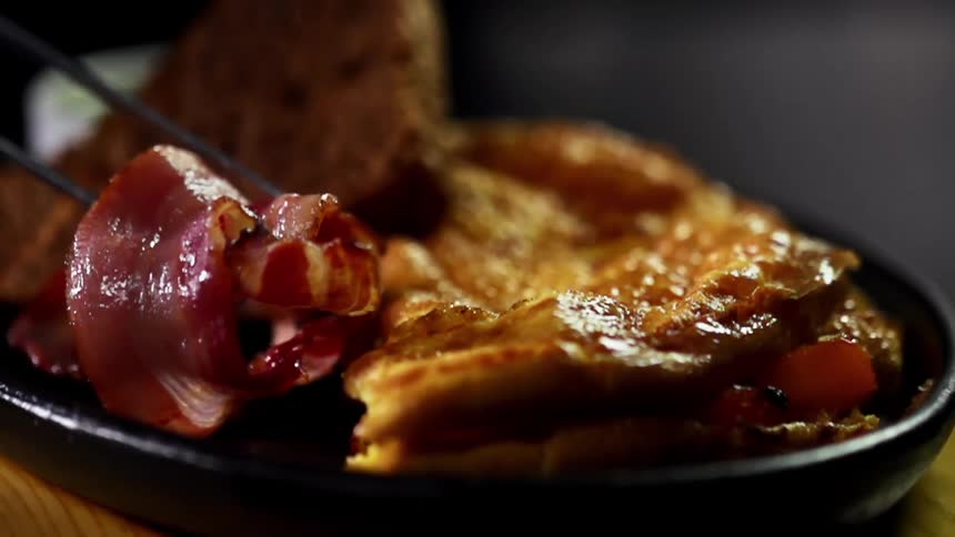 Metal tongs lower pieces of bacon onto a breakfast plate