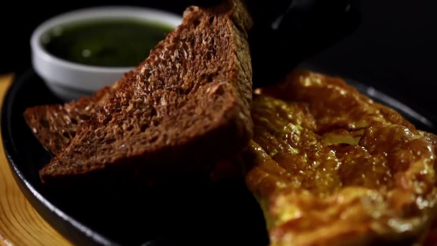 Person adds toast to plate holding omelet and sauce