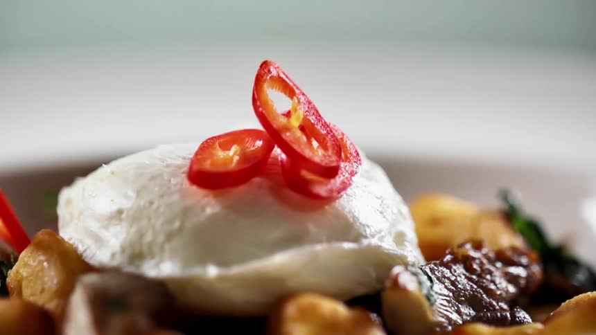 Several slices of chopped red jalapeno pepper are dropped onto the top of a poached egg