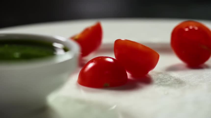 Red small diced tomatoes roll over a ceramic white dish near green sauce