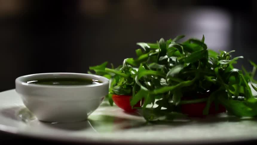 Tomatoes and greens drop onto a white dining plate