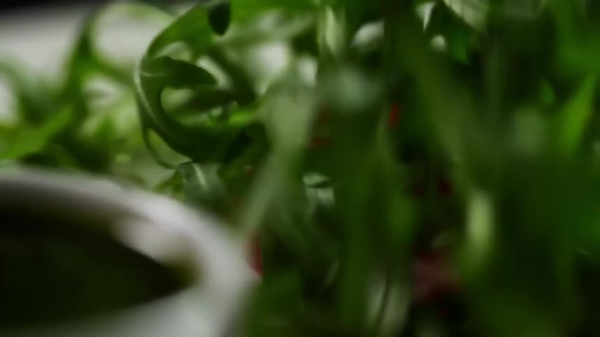 Three cherry tomatoes atop a glass plate have a pile of arugula dropped onto them