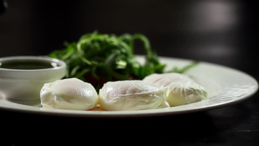Chef wearing black latex gloves serves poached eggs in a white ceramic dish