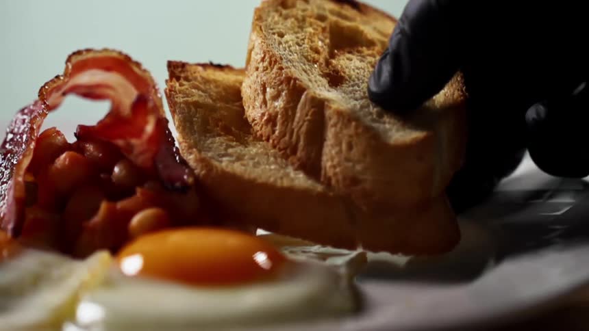 A gloved hand places two pieces of toast on a breakfast plate