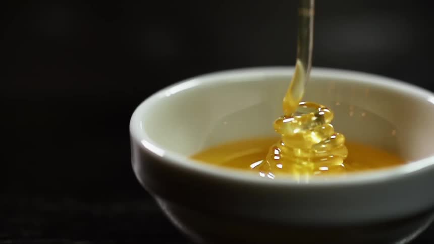 Honey pours into a small white bowl