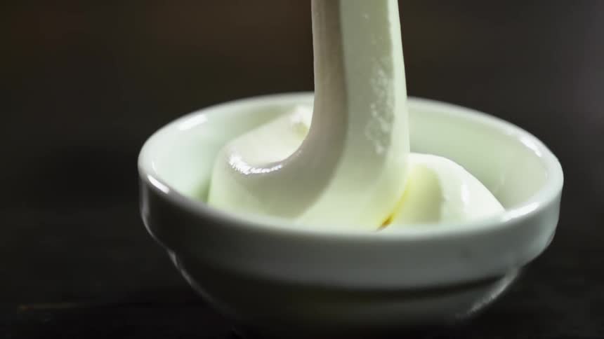 A small glass bowl is slowly filled with thick white cream