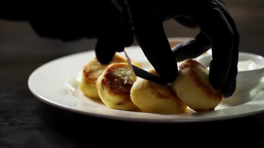 Chef wearing black latex gloves places small pastries over a white ceramic plate near creams