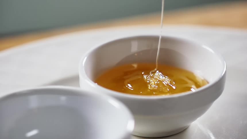 Honey pours into a small white bowl