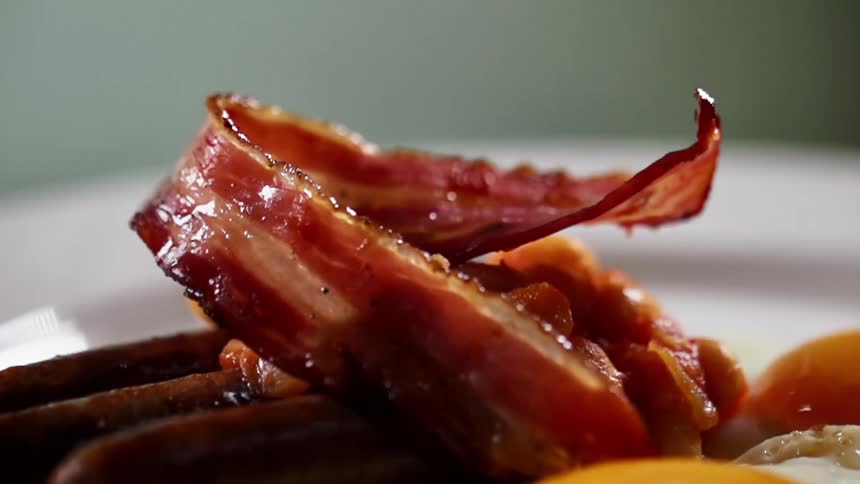 A piece of cooked bacon is placed atop a plate of sausages