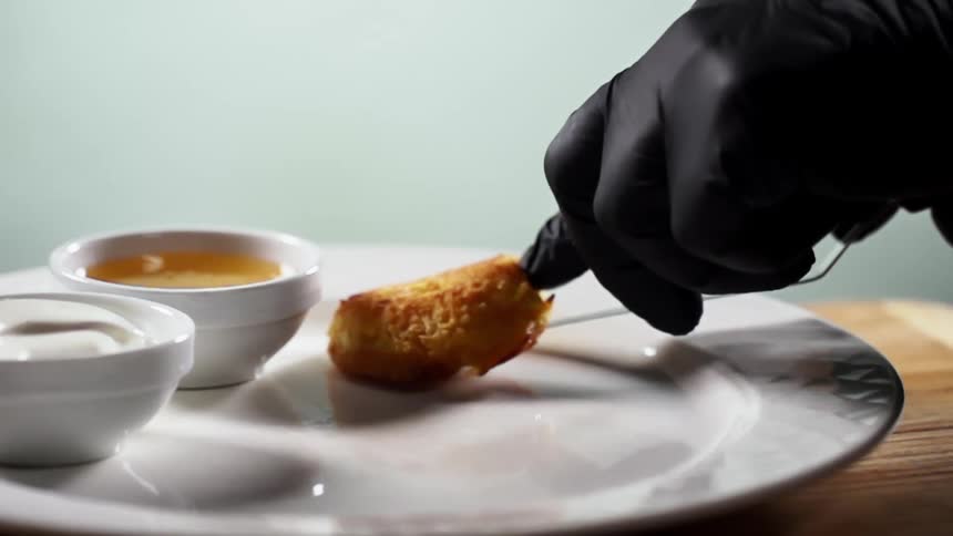 A person with gloves placing food on a plate with a spatula next to dipping sauce