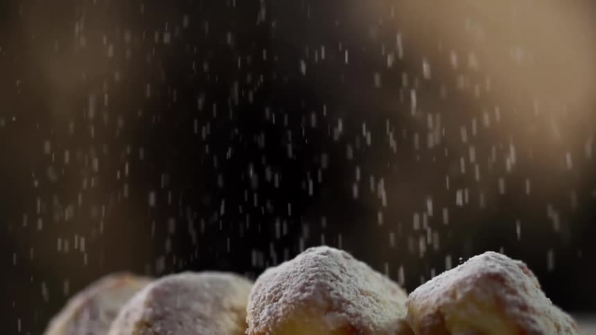 Several pastries are side by side while being sprinkles with a generous coating of powdered sugar
