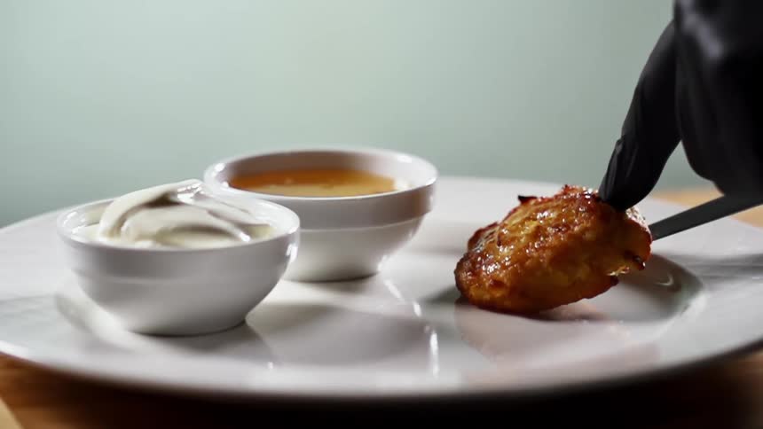 A black gloved hand places a piece of meat on a plate with dipping sauces