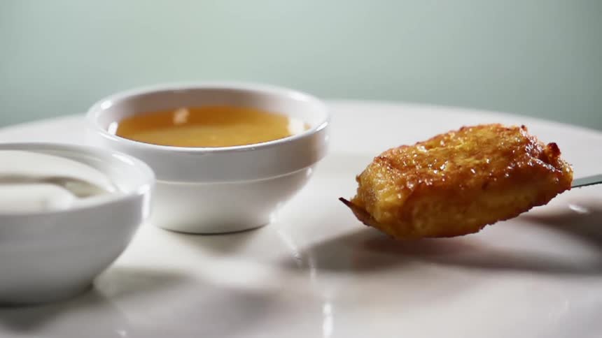 A breaded and fried patty is placed onto a plate which also has two small bowls of dipping sauce