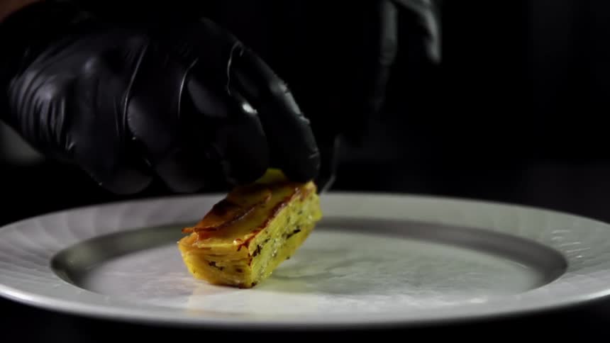 Slice of gourmet food being plated on a white ceramic dish