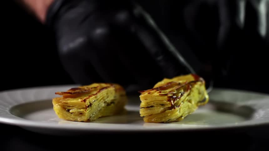 A person with gloves placing food on a plate with a spatula