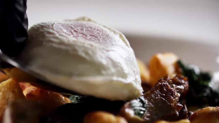 A cooked egg is placed on the dish of meat and potato
