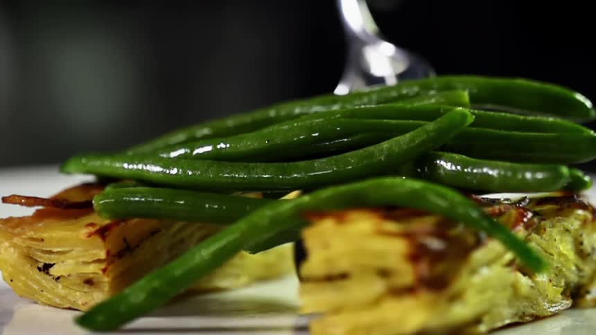 A spoon drops a pile of green beans on a plate of food