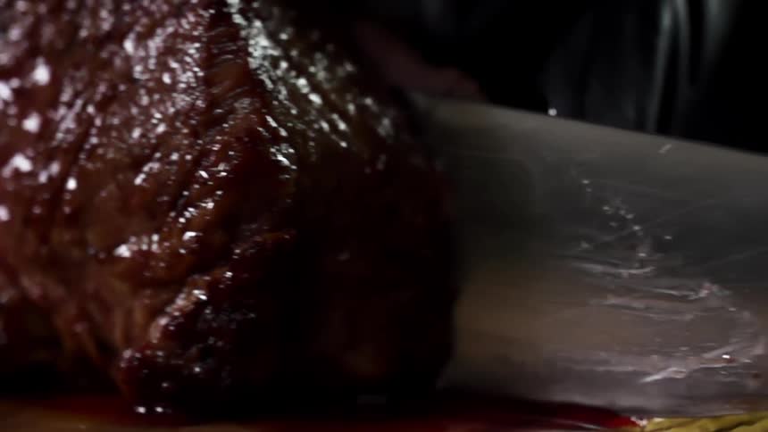 Close up of the hands wearing black gloves cutting a juicy steak