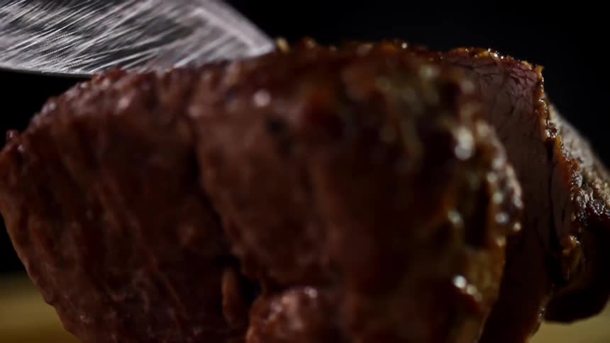 Juicy steak is being cut in half by a sharp knife