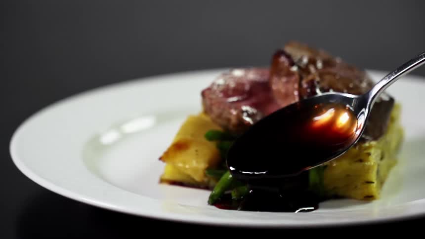 A spoon drops sauce on a plate