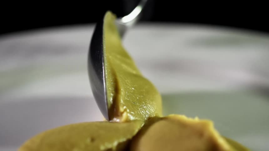 A spoon filled with a thick green sauce is lowered and carefully placed on a large pile of the sauce