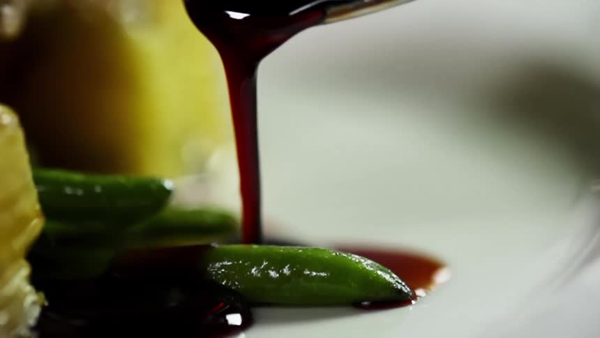 Dark thick sauce covers cooked green beans in a white ceramic dish