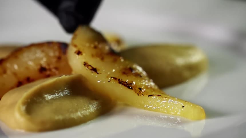 A grilled vegetable is placed on a white plate with a yellow sauce