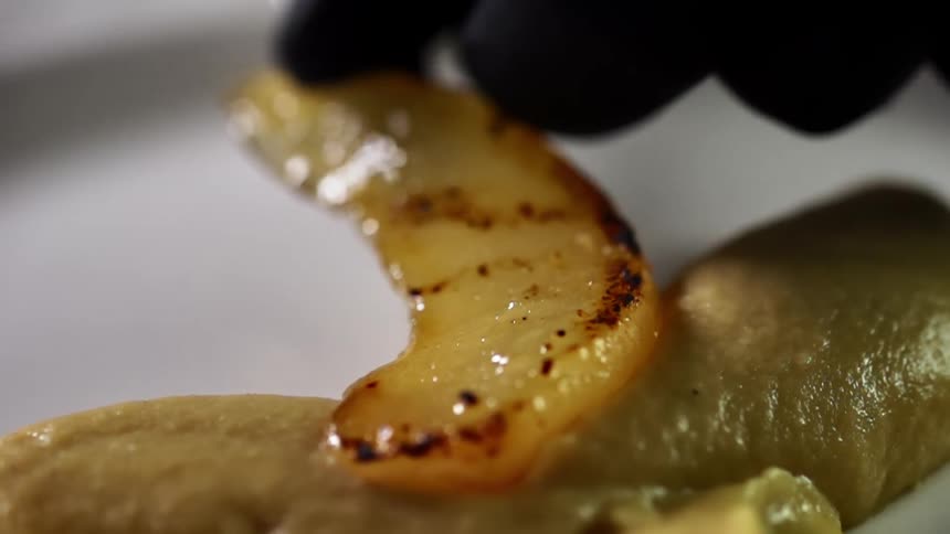 A person wearing a black glove sits a piece of cooked fruit on a plate