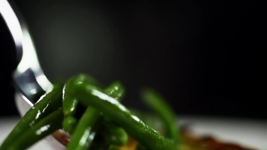 A utensil drops green beans on a meal plate