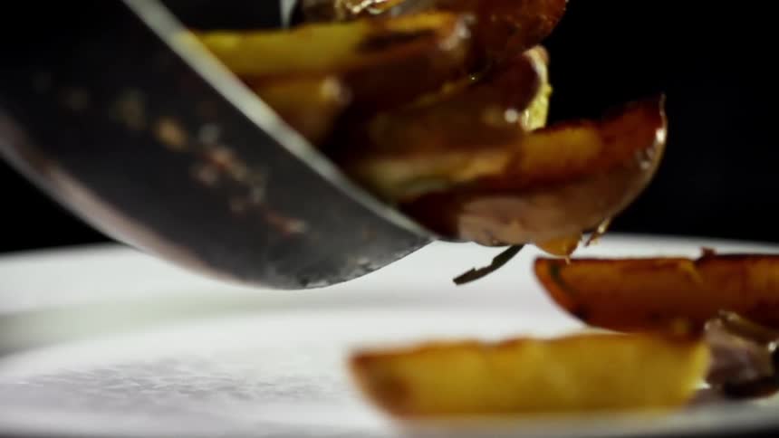 Sliced fried potatoes fall from a pan into a ceramic white dish