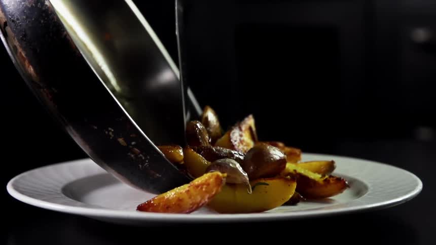 Grilled potato wedges are poured from a dark pan onto a plain white plate