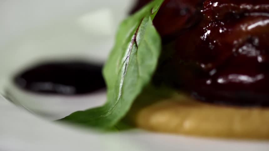 A mint leaf is placed against a purple puree on a white plate