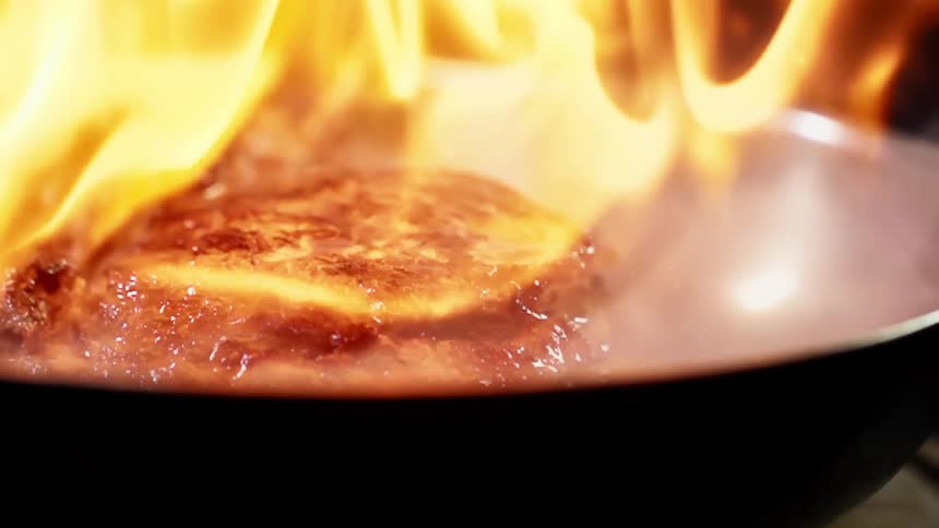 Steak is being cooked in a flaming pan