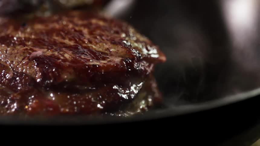 Juicy steak is being cooked in a black pan
