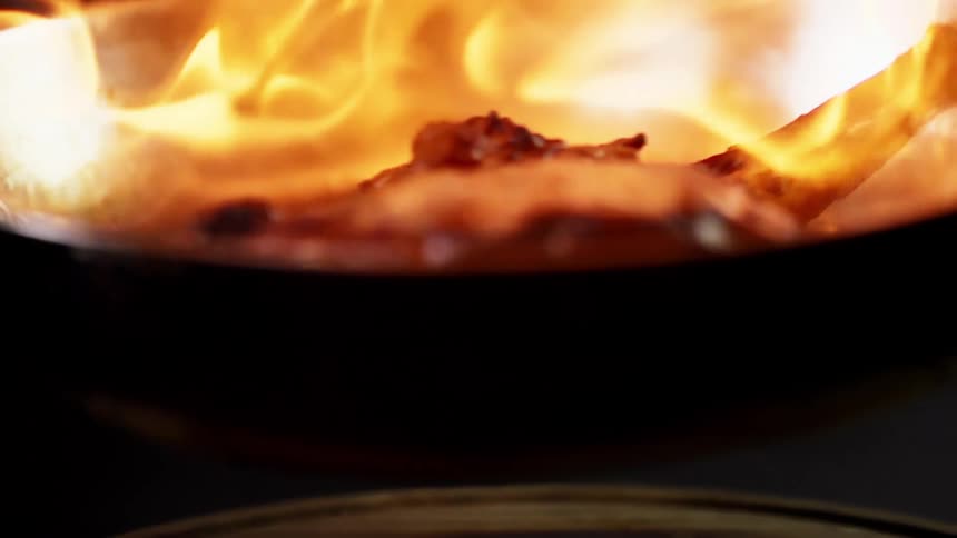 A piece of steak with the bone left is is seared using fire in a metal pan