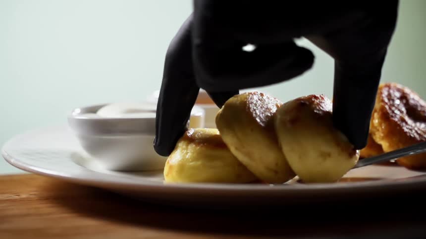 Baked goods are placed on a white ceramic plate by gloved hands