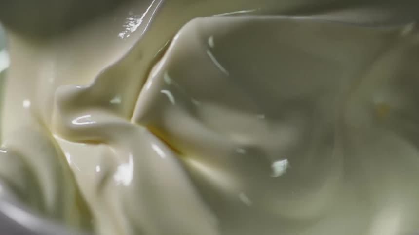 White shiny cream being served in a white ceramic bowl with a spoon