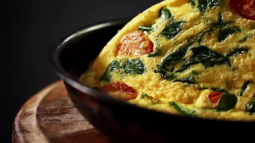 A vegetable omelette in a bowl gets flipped